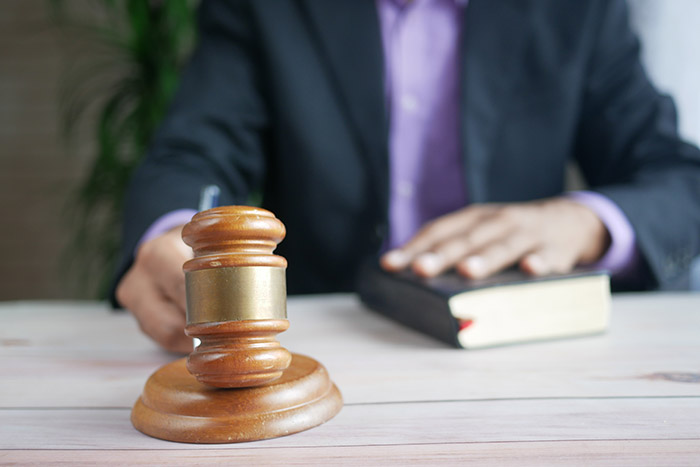 An image of a hand holding a gavel and another hand on the Bible